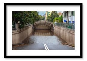 Flooded underpass blocks city road, with fallen leaves and rain-soaked asphalt in the foreground. Concept of flooding, stormwater, and dangerous road conditions