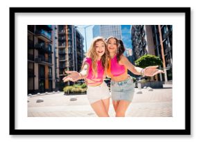 two happy friends pose in a sunny city street wearing bright pink crop tops and shorts enjoying a fun playful moment together in urban style and fashion