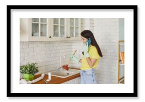 Woman standing near kitchen sink and making phone call to plumber, having problem of clogged sink, using plunger to unclog, wearing protective rubber gloves. Housework problem concept 