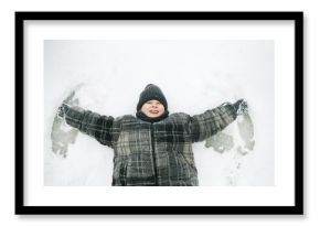 Caucasian child lying on snow making snow angel, smiling with arms outstretched, wearing winter clothing, looking up with joyful expression, winter outdoor activity