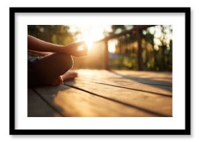 Person practices meditation on a wooden deck at sunset near trees and green nature