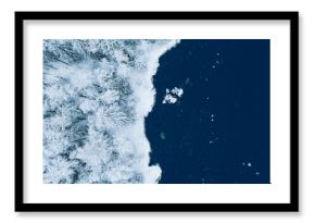 Aerial view of blue water sea and snow covered trees woods in winter Finland.