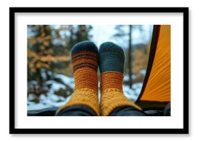 A pair of colorful knitted socks is seen resting comfortably inside a tent. Snow on the ground contrasts with vibrant autumn leaves in the background, creating a cozy camping atmosphere.