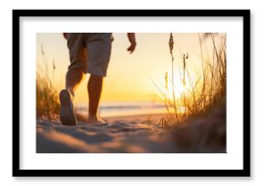 A person walks barefoot along a sandy beach path during a golden sunset. 