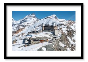 Aerial view of Gornergrat Observatory in Zermatt, Switzerland, with twin domes, snow covered Alps, Matterhorn peak, train station, and visitors below.