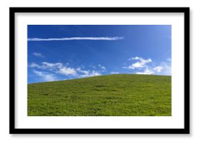 Vibrant green hill under a clear blue sky with wispy clouds and a jet trail i