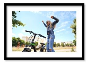 Schoolgirl jumping joyfully with raised hands near bicycle, celebrating freedom in sunlit urban park landscape