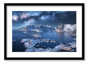 Aerial view of Milky Way arch, sea, village and snow covered mountains in winter at night. Lofoten Islands, Norway. Arctic landscape with starry sky, road, rorbu, houses, milky way, snowy rocks. Space
