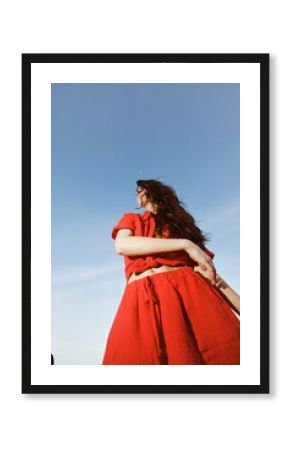Joyful Dancing by the Sea: A Smiling Woman Embraces Freedom and Fun in Trendy Red Summer Fashion, Surrounded by the Beautiful Beach and Blue Sky