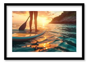 Legs of a young woman on a paddle surf in the sea at sunrise
