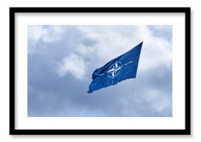 NATO flag on cloudy sky. Flying in the sky