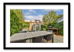 A stylish outdoor patio featuring a spacious wooden table surrounded by black chairs, set among lush greenery and blue skies. Ideal for gatherings and relaxation.