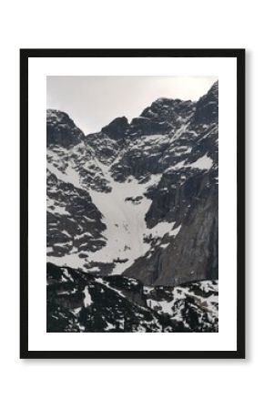 Steep, rugged Tatra mountain pass covered in snow lies between jagged cliffs and dark rocky slopes above a green ridge near Zakopane, Poland
