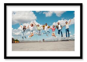 Group of cheerful friends jumping together outdoors during a sunny day, showcasing friendship and youthful energy