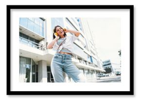 Young woman enjoying music outdoors in urban setting, smiling in casual outfit