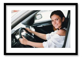 Smiling young woman driving car in daylight, enjoying her ride through the city streets