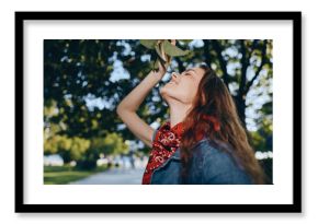 smiling woman enjoying nature outdoors in sunny park with green trees and casual denim jacket and red scarf accessory