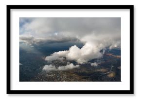 Aerial view from airplane window at high altitude of distant city covered with puffy cumulus clouds forming before rainstorm