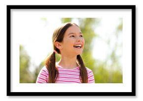 Cheerful young girl with brown hair outdoors enjoying a sunny spring day, dressed in a striped casual shirt and smiling joyfully