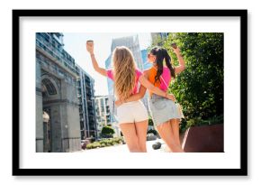 Two young friends walk in a sunny city street enjoying a fashionable day out and sharing a hug while exploring urban life with confidence and style