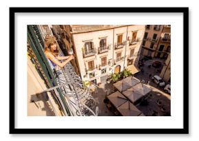 Woman enjoying a peaceful morning on a balcony in Palermo, overlooking old Sicilian buildings under the warm Mediterranean sun. Authentic slow living vibe
