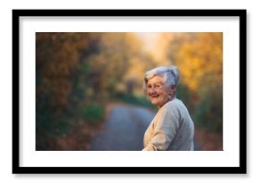 Senior woman walking outdoors in autumn forest.