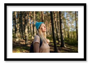 Calm happy woman hiking alone in woods, exploring nature, taking forest bath, calming mind and relieving stress at sunset. Female standing in woodland under sunlight and smiling, mindfulness practice