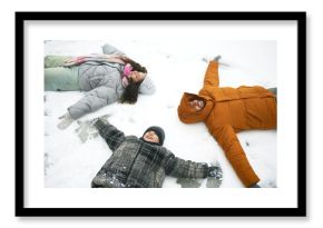 Caucasian man, woman and child lying on snow making snow angels, smiling and looking up, winter outdoor activity, family enjoying time together