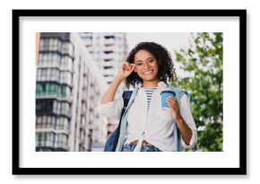 Young woman with glasses holds coffee on city street smiling outdoor urban lifestyle portrait beside modern buildings