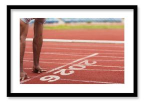 A runner crouches at the starting line of a track, getting ready to sprint. The clean red surface and numbered lanes reveal an active sports environment on a bright day.