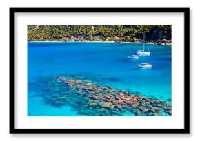 Rocks and stones in crystal clear turquoise sea water of Agios Nikitas bay with sailing boats, Lefkada island, Greece