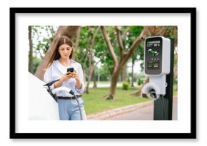 Young woman using smartphone online banking application to pay for electric car battery charging from EV charging station during vacation holiday road trip at national park or summer forest. Exalt