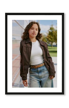 Vertical portrait of teen girl in casual clothes leaning on metal fence during taking photo