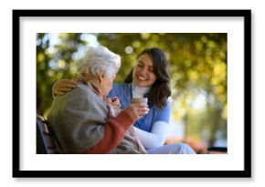 Elderly woman enjoying cup of coffee with her nurse in the park during warm autumn day. Young caregiver spending time with senior woman.