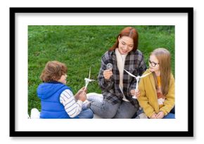 Woman volunteer teaching group of children explaining how wind turbines produce renewable energy