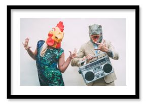 Crazy senior couple wearing chicken and t-rex mask while dancing outdoor - Mature trendy people having fun celebrating and listening music with boombox - Absurd concept of masquerade funny holidays