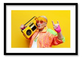 funny crazy old granny with tape recorder in sports hipster clothes listens to rock music on yellow background