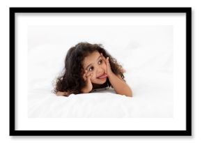 Funny little girl lying on stomach on bed making funny face