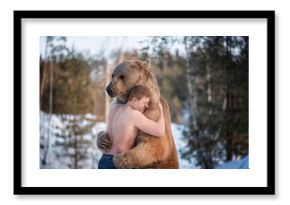 Half-naked man hugs a brown bear in a winter forest. Bear hugs man in response. The theme of the friendship of man and animal.