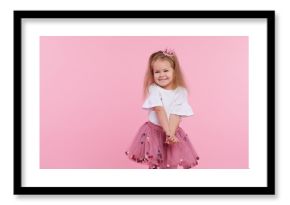 A cheerful little girl with in a tulle skirt and princess crown on her head isolated on a pink background. Celebrating a vibrant carnival for kids, birthday party, having fun 