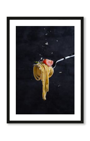 tagliatelle with tomato and pesto on fork. Italian food. Dark background