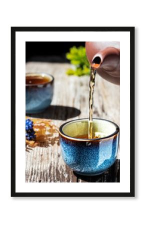 Hot green tea is poured from the teapot into the blue bowl, vintage wooden table, steam rises above the cup. Tea leaves next to the cup. Close-up, tea ceremony, minimalism