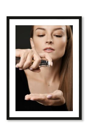 Young pretty woman model pouring hait styling cosmetics to hand for making hairstyle of gorgeous silky long straight hair over dark background. Hairstyle, hairsalon, hairdresser, fashion concept