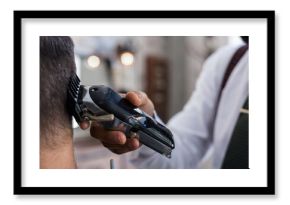 Close up of cropped unrecognizable stylish dandy ethnic male barber trimming hair of adult client with electric clipper in hairdressing salon