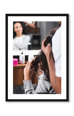 African american hairdresser on blurred foreground touching curly hair of client