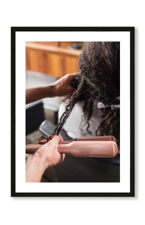 Cropped view of african american hairdresser holding hair straightener near client