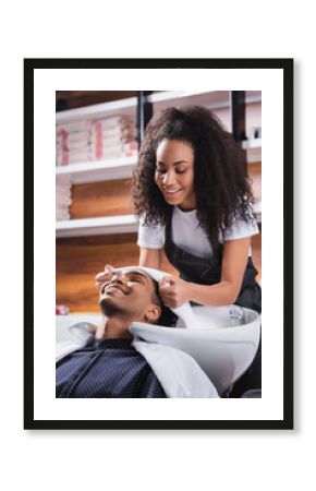 Smiling african american hairdresser holding towel near head of client in salon