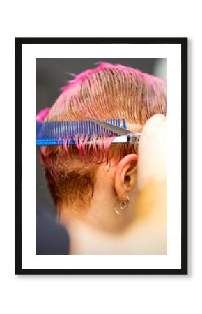 Young caucasian woman with pink hair getting a short haircut by a male hairdresser's hands in a hairdressing salon