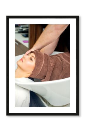 Gorgeous young relaxed woman getting her wet hair wrapped in a towel after washing by a professional hairdresser at the beauty salon