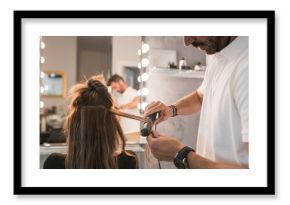 Male hairdresser using straightener on female customer's hair at salon